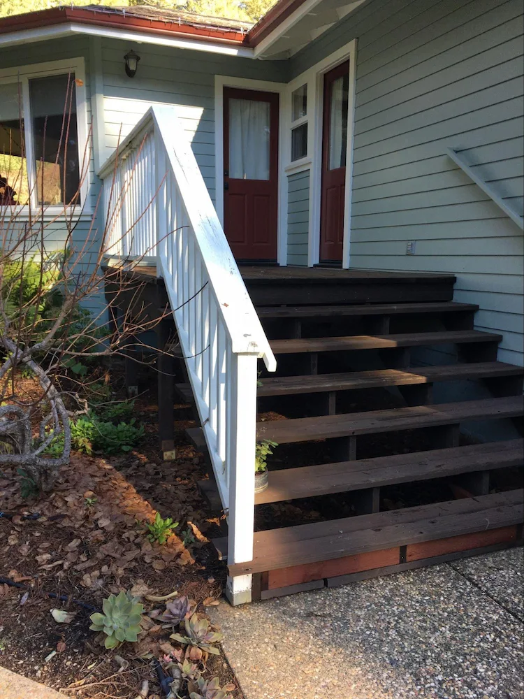 Softwood stairs and side deck.  Exterior stairs share similar wildfire vulnerabilities and mitigations as decks.  Note the lowest step has been retrofitted with multiple combustible wood boards to create a vertical fascia, which creates an ember ignition vulnerability similar to that addressed in the siding clearance section; better to remove the softwood fascia in this case.