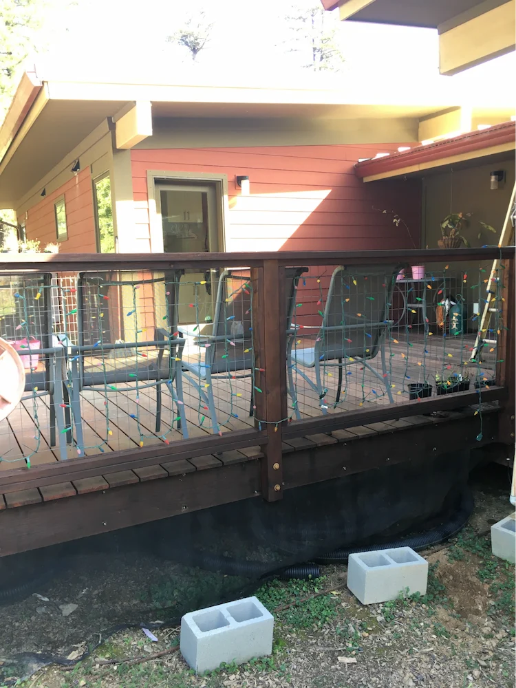 Softwood deck with less than 24 inches of ground clearance and vinyl coated fiberglass mesh screening installed. Note the area on the right where the screening has been pulled back and the combustible plastic hoses stored underneath. This screening example would be ineffective and noncompliant.