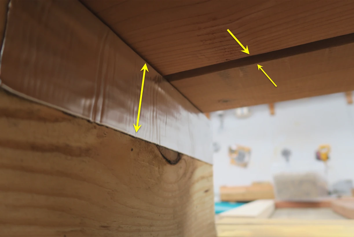 Photo of the underside of a small deck in a test environment. The gap between deck boards is 1/4 inch. Foil-faced bitumen tape is shown applied to the joist.