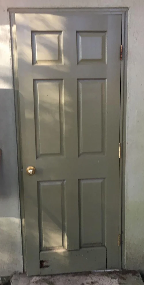 Outswing wood door with 3 inch hole and weathering damage on the lower rail