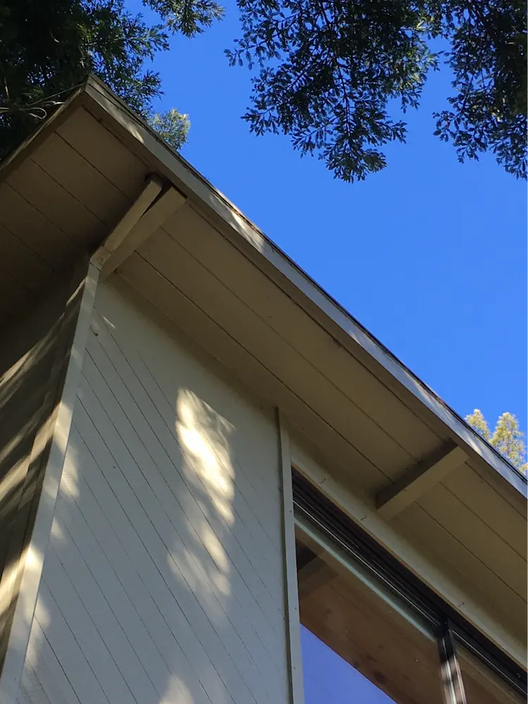 An open eave design on an unvented flat (~1:12) roof. Because the rafter tails are widely spaced and two stories off the ground, it is not a priority and should be rated compliant.