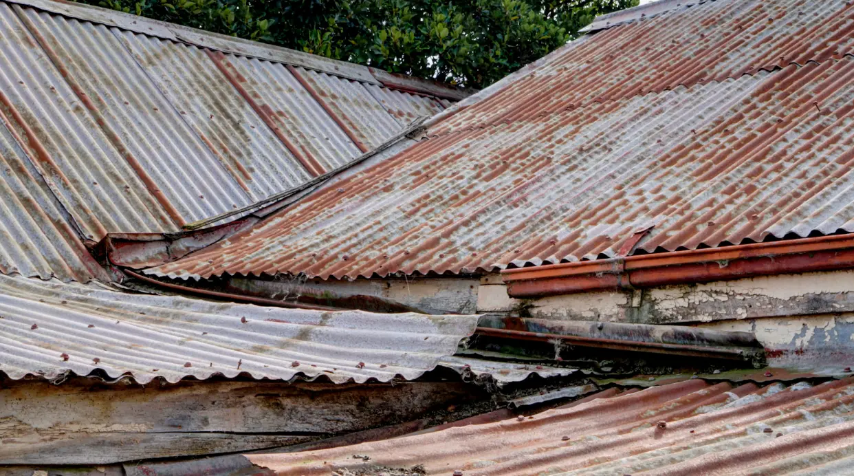 A complex corrugated metal roof with advanced rust and uplift. This roof should be replaced.